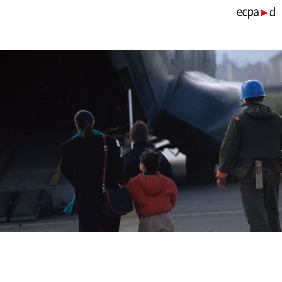 Vue de dos d'une femme et deux enfants accompagnés par un casque bleu lors de l'évacuation de blessés légers et de malades civils vers la France sur l'aéroport de Sarajevo.