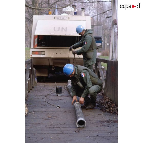 Casques bleus français raccordant des canalisations au camion-pompe de l'ONU pour le remplissage de bacs souples et citernes depuis un cours d'eau.