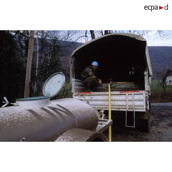 Près d'une citerne moilen un casque bleu du régiment d'infanterie chars de marine (RICM) supervisant le remplissage d'un bac souple dans un camion avec de l'eau pompée dans une rivière.