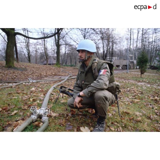 Un casque bleu du régiment d'infanterie chars de marine (RCIM) surveille le raccordement de tuyaux lors du remplissage de bacs souples et de citernes d'eau pompée dans une rivière.