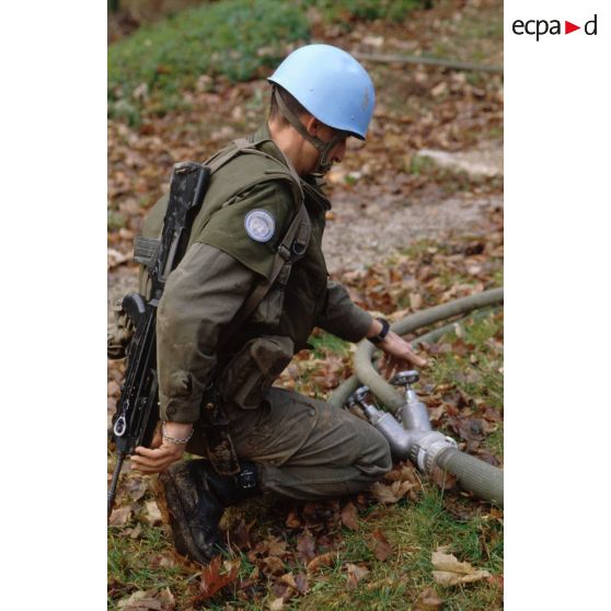 Un casque bleu du régiment d'infanterie chars de marine (RCIM) ajuste le raccordement de tuyaux lors du remplissage de bacs souples et de citernes d'eau pompée dans une rivière.