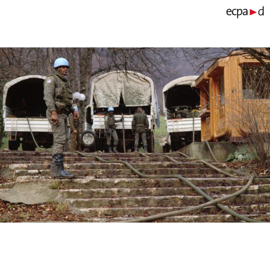 Casque bleu du régiment d'infanterie chars de marine (RICM) supervisant le remplissage de bacs souples dans des camions avec de l'eau pompée dans une rivière.