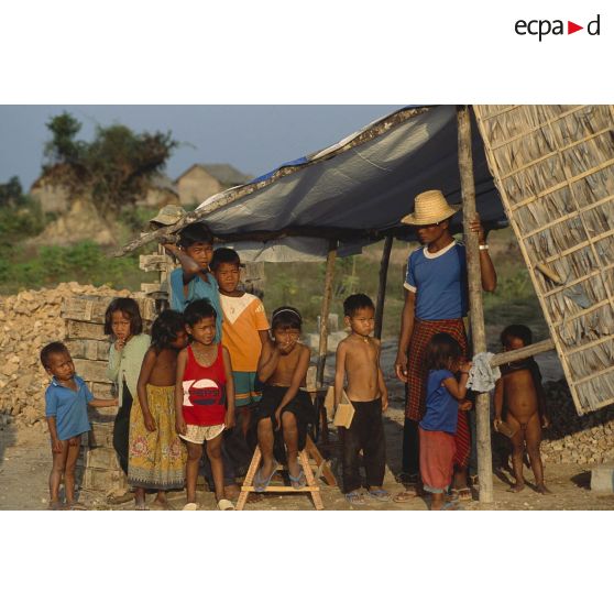 Groupe d'enfants avec un adulte devant une habitation en construction dans un village de réfugiés près de Siem Reap.