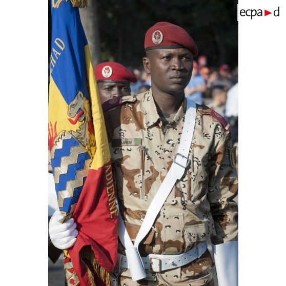 Portrait d'un soldat de la garde nationale et nomade du Tchad (GNNT) portant le drapeau des forces armées tchadiennes sur les Champs-Elysées à Paris.