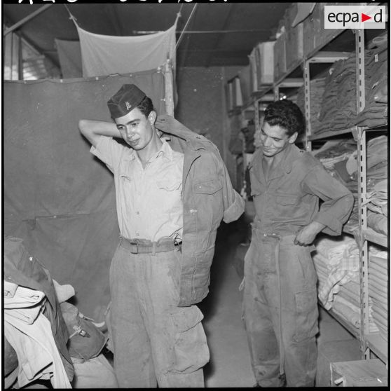 Portrait d'un jeune harki qui enfile sa tenue à l'intérieur du magasin d'habillement de Palestro.