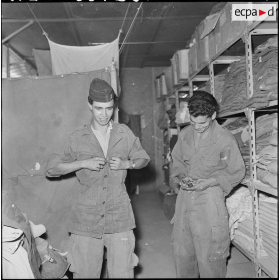 Portrait d'un jeune harki qui enfile sa tenue à l'intérieur du magasin d'habillement de Palestro.