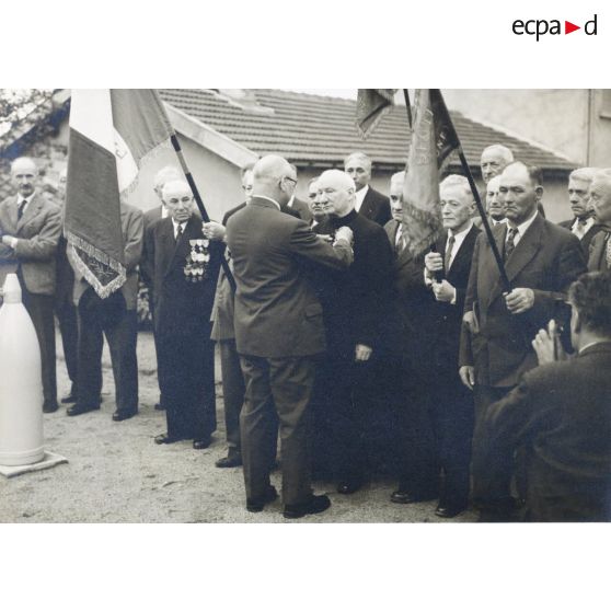 75. Remise de la légion d'honneur à M. l'Abbé Loys Roux par son frère chevalier le 28 août 1960 au monument aux morts des deux guerres à Chénas Rhône. [légende d'origine]