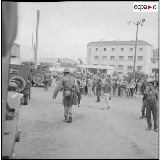 [Enfants regardant des soldats et un convoi de véhicules militaires progressant dans les rues d'Oran.]