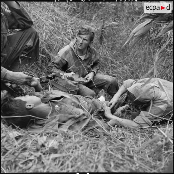 Le médecin-lieutenant Patrice Le Nepvou de Carfort  du 8e bataillon de parachutistes de choc (BPC) apporte les premiers secours à un parachutiste autochtone blessé au cours d'une reconnaissance au nord de Diên Biên Phu.