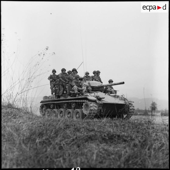 Progression d'un char M24 Chaffee de l'escadron de marche du 1er régiment de chasseurs à cheval (RCC) transportant des fantassins au cours d'une offensive contre des positions de l'Armée populaire vietnamienne à Diên Biên Phu.