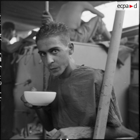 Portrait d'un prisonnier libéré par le Vietminh en train de boire dans un bol à bord d'un chaland de débarquement le rapatriant vers Haïphong.