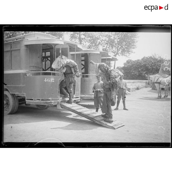 [Deux hommes embarquent des pièces de viande dans un camion, sous le regard d'autorités militaires.]