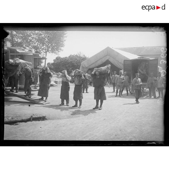 [Des hommes embarquent des pièces de viande dans un camion, sous le regard d'autorités militaires.]