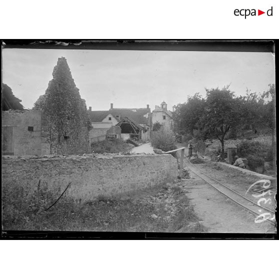 [Des soldats réparent une voie Decauville, qui passe à travers un village en ruine.]