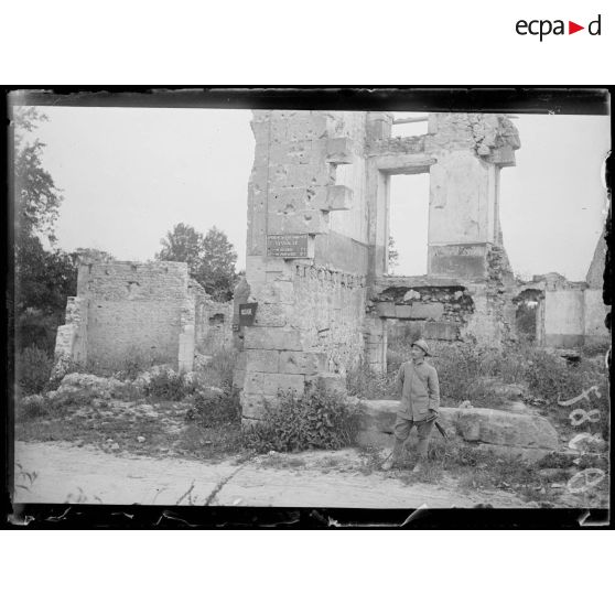 [Un soldat se tient debout devant une maison en ruine, à Vassogne.]