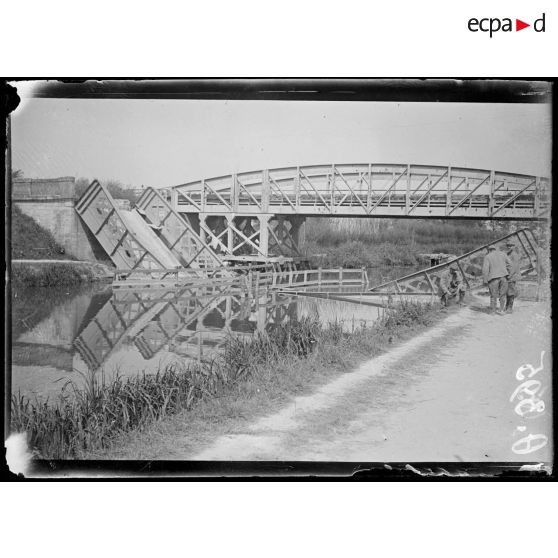 [Des soldats sont réunis devant un pont détruit.]