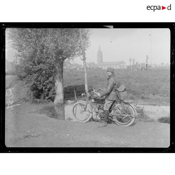 Roesbrugge. Vaguemestre sur motocyclette. Au fond l'église de Roesbrugge. [légende d'origine]