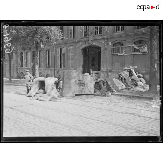 [Deux soldats devant une barricade composée de matelas, portes, chariots et table dans une rue de la ville de Reims.]