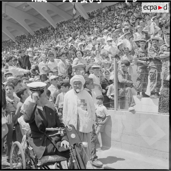 Un ancien combattant arbore avec fierté ses décorations parmi la foule au stade d'Oran pour la venue du général Salan, du général Massu et de Jacques Soustelle.