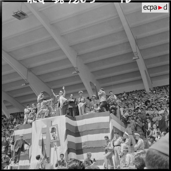 Depuis la tribune officielle du stade d'Oran, le général Salan lève les bras pour répondre aux ovations de la foule.