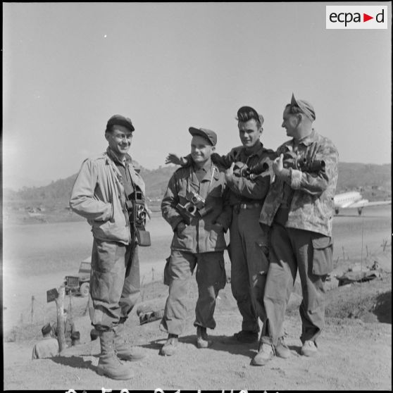 Photographie de groupe des reporters de la section ciné-photo du Service presse information (SPI) Jean Péraud, Paul Corcuff, André Lebon et Pierre Schondoerffer devant le terrain d'aviation de Na San.