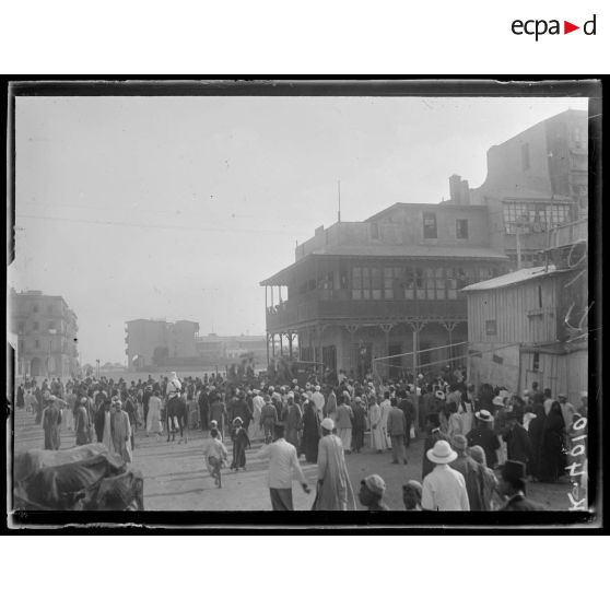 Port-Saïd, 7 h 20. La foule près d'un trou de bombe. A droite, le café près duquel la bombe est tombée (6 morts). [légende d'origine]