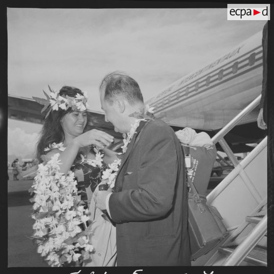 Un passager, arrivant à Faa'a, l'aéroport de Papeete, se voit offrir un collier de fleurs par une hôtesse polynésienne en tenue traditionnelle.