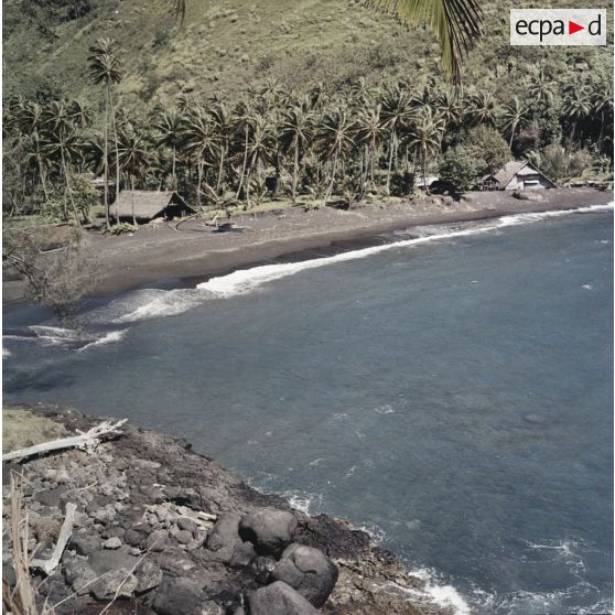 Paysage du littoral à Tahiti, habitations traditionnelles bordant une plage de sable noir.