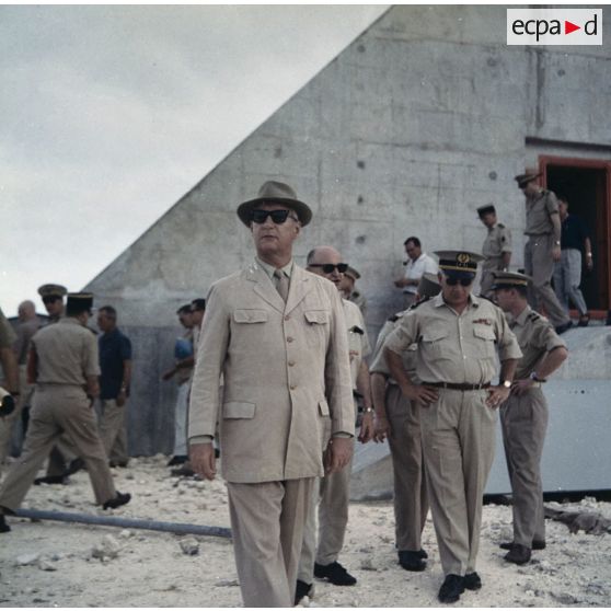 Pierre Messmer, ministre des Armées, sort du bunker d'un poste d'enregistrement avancé (PEA) [Denise ou Dindon] sur l'atoll de Moruroa. En arrière-plan, Robert Hirsch, délégué du gouvernement auprès du Commissariat à l’énergie atomique (CEA), discute avec un contre-amiral.