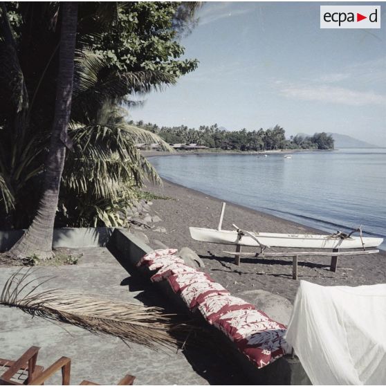 Plage de l'hôtel Royal Tahitien à Papeete. Une pirogue à balancier est posée sur des poteaux sur le rivage. En arrière-plan, l'île de Moorea.