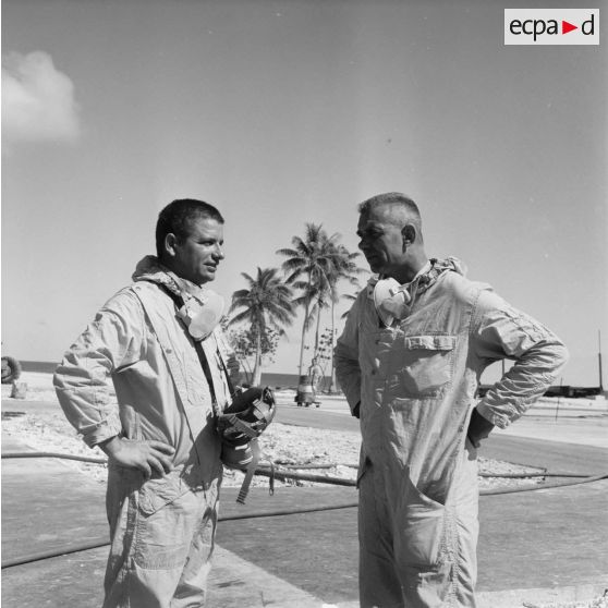 Sur une aire de lavage du service de décontamination de Hao, discussion en tenue de protection après un tir d'essai nucléaire entre un personnel de l'équipe et le commandant André Darret, directeur de l'Etablissement cinématographique des armées (ECA), en mission de tournage.