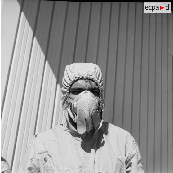 Devant un hangar du service de décontamination de Hao, portrait d'un personnel en tenue de protection portant un masque antipoussière.