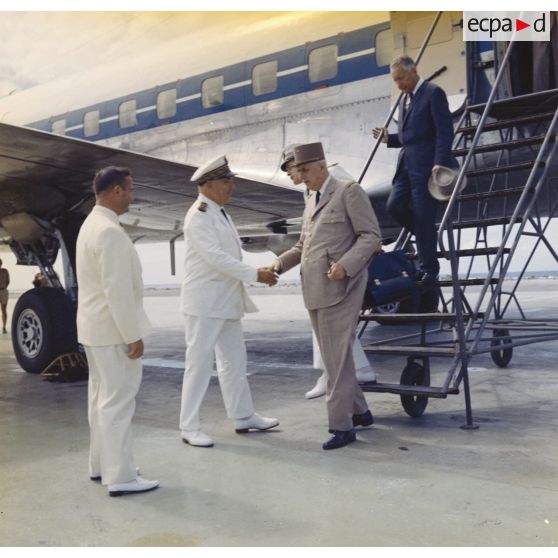 Le général Charles De Gaulle, président de la République, suivi de son aide de camp et de Pierre Messmer, ministre des Armées, au pied de la passerelle de l'avion à l'aéroport de Moruroa, accueilli par Jean Viard, directeur des essais, et le vice-amiral d’escadre Jean Lorain, commandant du groupe opérationnel des expérimentations nucléaires (GOEN).