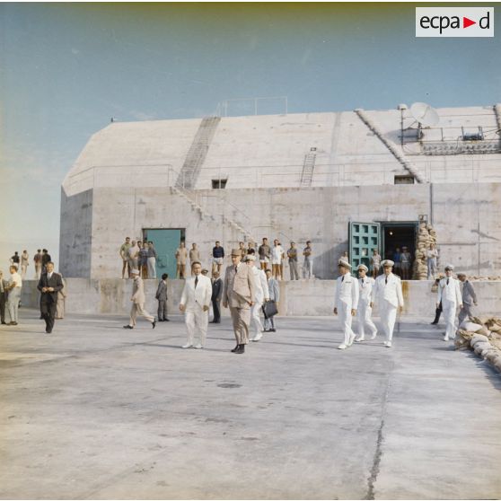 Aux côtés de Jean Viard, directeur des essais, le général Charles De Gaulle, président de la République, sort du bunker du poste d'enregistrement avancé (PEA) Denise, en présence du vice-amiral Jean Lorain, commandant du groupe opérationnel des expérimentations nucléaires (GOEN).