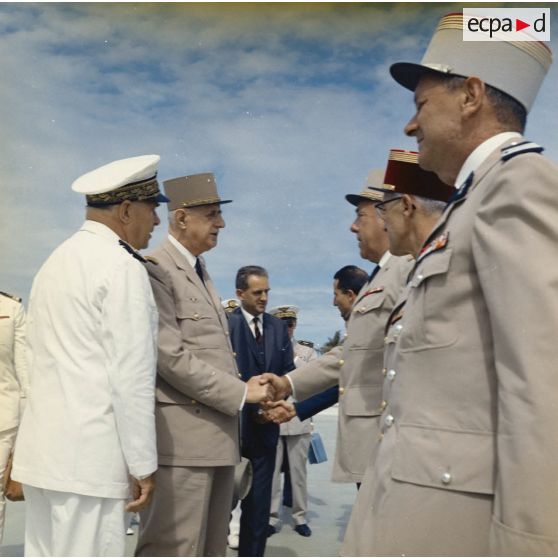 Le général Charles De Gaulle, président de la République, se fait présenter par le vice-amiral Jean Lorain, commandement du groupe opérationnel des expérimentations nucléaires (GOEN), les officiers supérieurs du site, en présence d'Alain Peyrefitte, ministre de la Recherche scientifique et des Questions atomiques et spatiales.