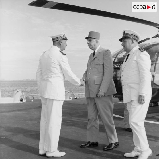 Le général Charles De Gaulle, président de la République, est accueilli à bord par le capitaine de vaisseau Michel Teisserenc, commandant du croiseur De Grasse, avec le vice-amiral Jean Lorain, commandant du groupe opérationnel des expérimentations nucléaires (GOEN).