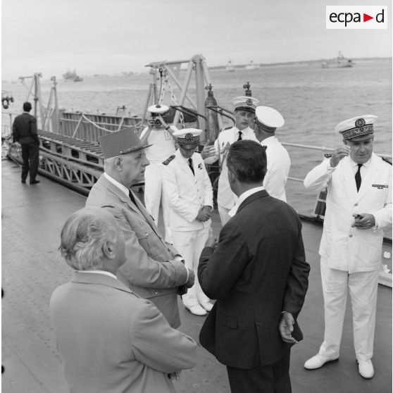 Le général Charles De Gaulle, président de la République, avec Alain Peyrefitte, ministre de la Recherche scientifique et des Questions atomiques et spatiales, et Pierre Billotte, ministre des Départements et territoires d'Outre-mer, en présence du vice-amiral Jean Lorain, commandant du groupe opérationnel des expérimentations nucléaires (GOEN), à bord du croiseur De Grasse.