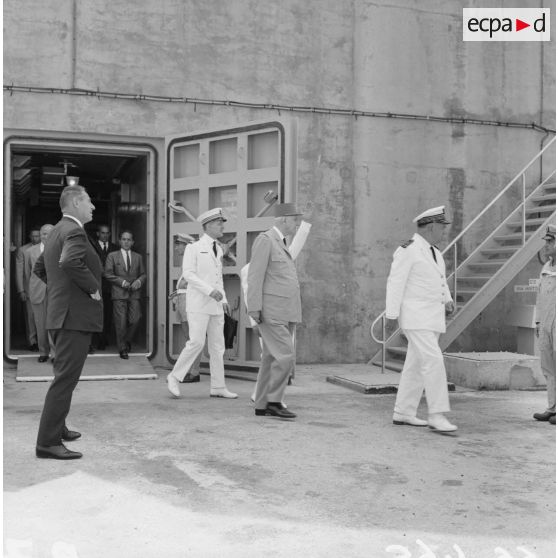 Le général Charles De Gaulle, président de la République, sort du bunker du poste d'enregistrement avancé (PEA) Denise, en compagnie du vice-amiral Jean Lorain, commandant du groupe opérationnel des expérimentations nucléaires (GOEN).