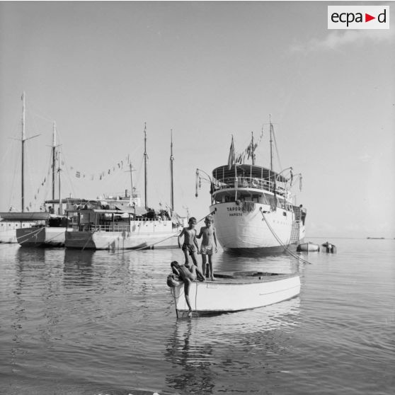 La goélette Taporo dans le port de Papeete, au premier plan des enfants jouant sur une barque, 1964.