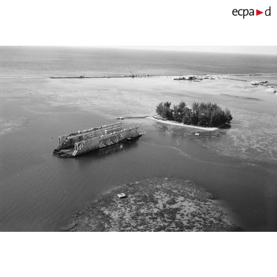 Vue du dock flottant de la marine nationale et de l'îlot Motu Uta dans le port de Papeete (Tahiti), 1964. Chantier de construction de quai d'amarrage en palplanches d'acier et digue en arrière-plan.