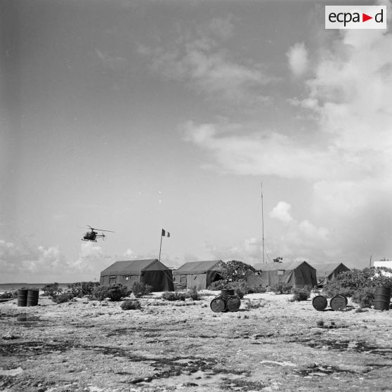 Atterrissage d'un hélicoptère Alouette II au camp de tentes sur un motu. Construction du site de Moruroa.