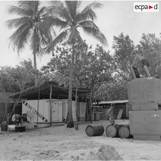 Infrastructures de la zone de vie. Peut-être sur l'atoll d'Hao. Derrière les cuisines : cuisinier lavant les gamelles, chambres froides ISO FRIGO, bonbonnes de gaz , citernes d'eau.