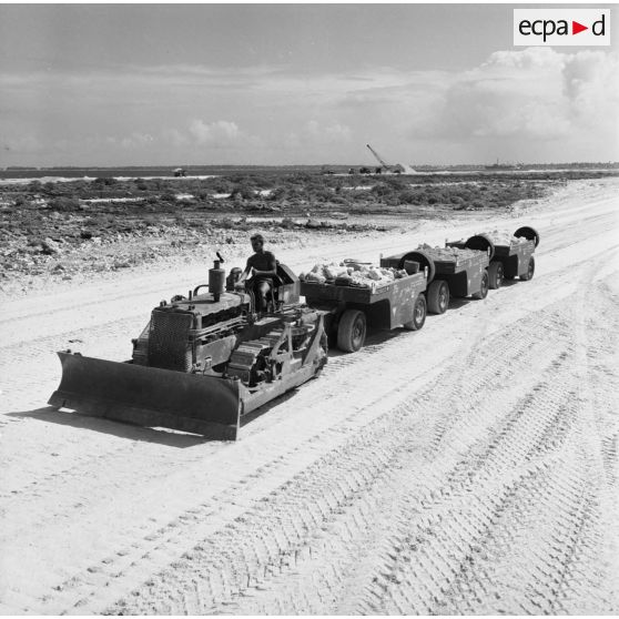 Engin tractopelle chenillé du génie avec remorques sur roues transportant des minéraux concassés pour le terrassement. Peut-être sur l'atoll de Moruroa.