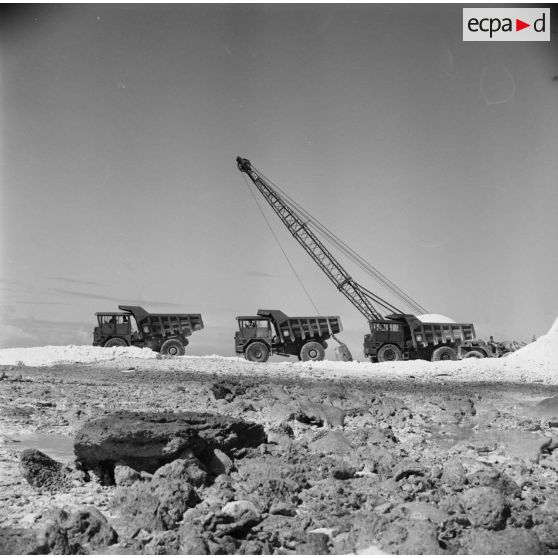 Camions à bennes et engin de levage pour le terrassement. Peut-être sur l'atoll de Moruroa.