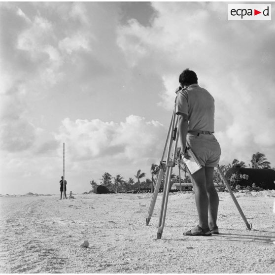 Des géomètres font un relevé du terrain sur un chantier de construction de piste. Peut-être sur l'atoll de Moruroa.