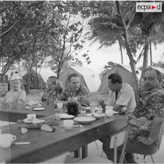 Hommes politiques polynésiens déjeunant : de gauche à droite Alfred Poroï, maire de Papeete, Jacques Tauraa, président de l'Assemblée territoriale, Charles Poroï ?, Jean Roy Bambridge, conseiller municipal de Papeete, lors d'une visite à Moruroa sur le site du centre d'expérimentation du Pacifique (CEP) en construction, vers fin février-fin avril 1964.