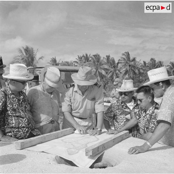 Hommes politiques polynésiens : Jacques Tauraa, président de l'Assemblée territoriale, Alfred Poroï, maire de Papeete, Jean Roy Bambridge, conseiller municipal de Papeete, écoutant l'exposé d'un capitaine de vaisseau autour d'une carte de l'atoll lors d'une visite à Moruroa sur le site d'expérimentation en construction, vers fin février-fin avril 1964.