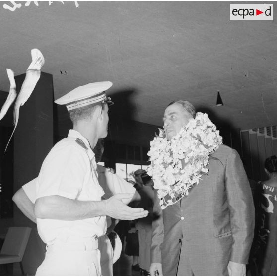 Arrivée du contre-amiral Jacques Thabaud, nouveau directeur du Centre d'expérimentations du Pacifique (CEP), accueilli avec des colliers de fleurs, en présence d'un officier à l'aéroport de Faa'a, 1964.