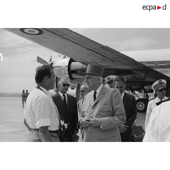 Le général Charles De Gaulle, président de la République, discute avec un photographe, en présence de Pierre Messmer, ministre des Armées, au pied de l'avion à l'aéroport de Moruroa. En arrière-plan, Pierre Billotte, ministre des Départements et territoires d'Outre-mer, et Alain Peyrefitte, ministre de la Recherche scientifique et des Questions atomiques et spatiales.