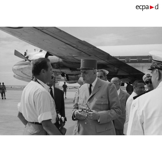 Le général Charles De Gaulle, président de la République, discute avec un photographe, en présence de Pierre Messmer, ministre des Armées, au pied de l'avion à l'aéroport de Moruroa. En arrière-plan, Pierre Billotte, ministre des Départements et territoires d'Outre-mer, et Alain Peyrefitte, ministre de la Recherche scientifique et des Questions atomiques et spatiales.